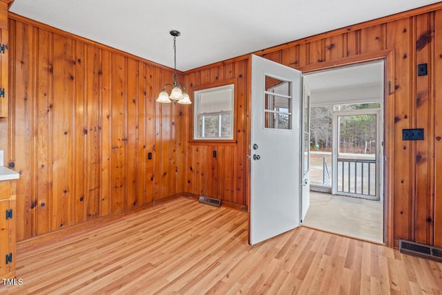 unfurnished dining area with light wood-style floors, wooden walls, visible vents, and an inviting chandelier