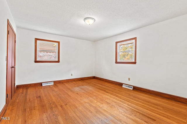 empty room featuring light wood-style floors, baseboards, visible vents, and a textured ceiling