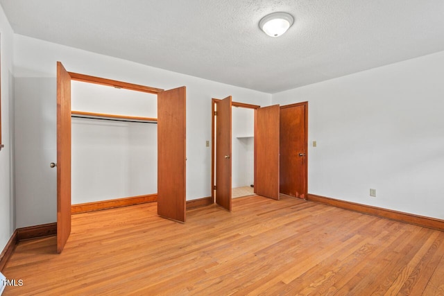 unfurnished bedroom with light wood-style flooring, a textured ceiling, baseboards, and a closet