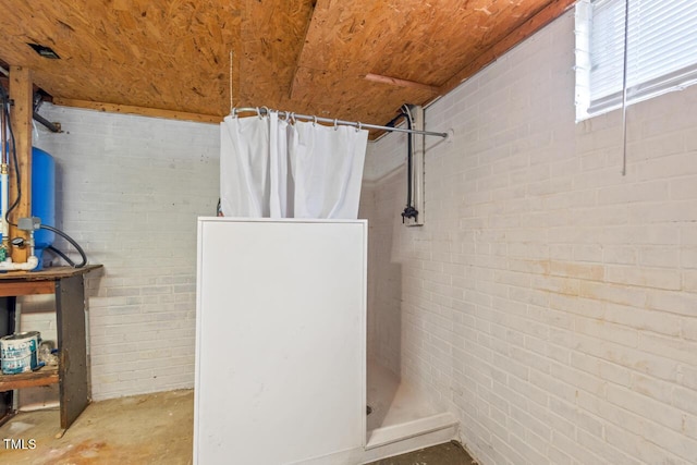 bathroom featuring brick wall, concrete floors, and tiled shower