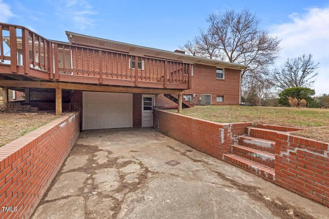 back of property with an attached garage, brick siding, driveway, a lawn, and a wooden deck