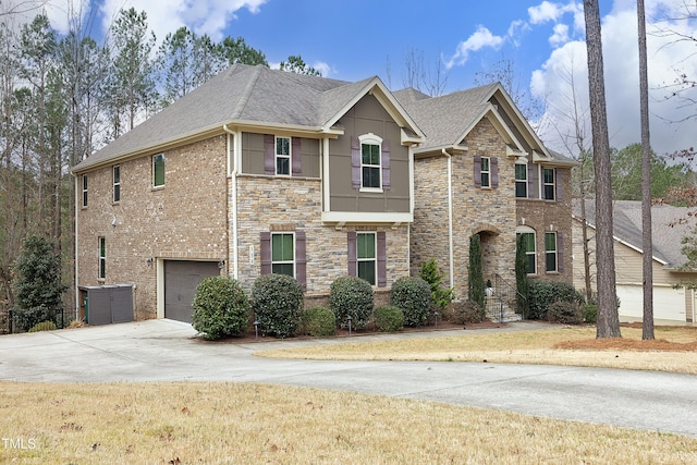 view of front of property with stone siding, a garage, driveway, and roof with shingles