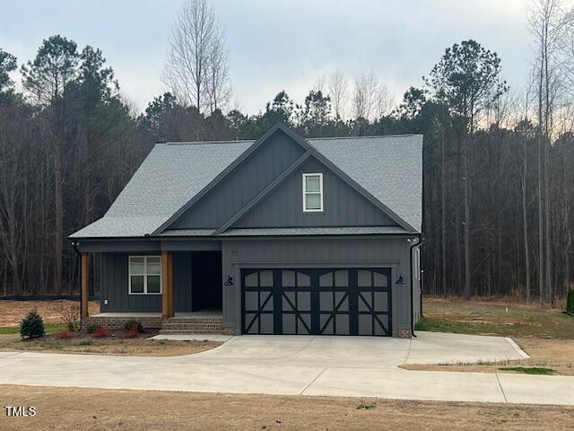 view of front facade with a view of trees, board and batten siding, covered porch, and driveway