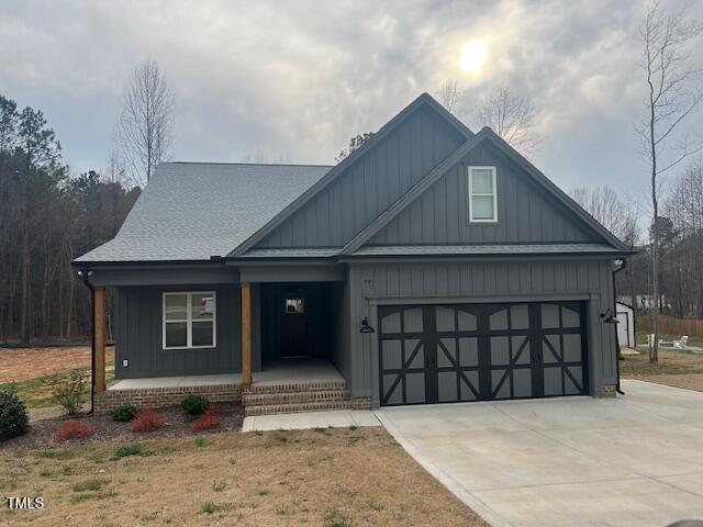 view of front facade with covered porch, board and batten siding, a shingled roof, and driveway