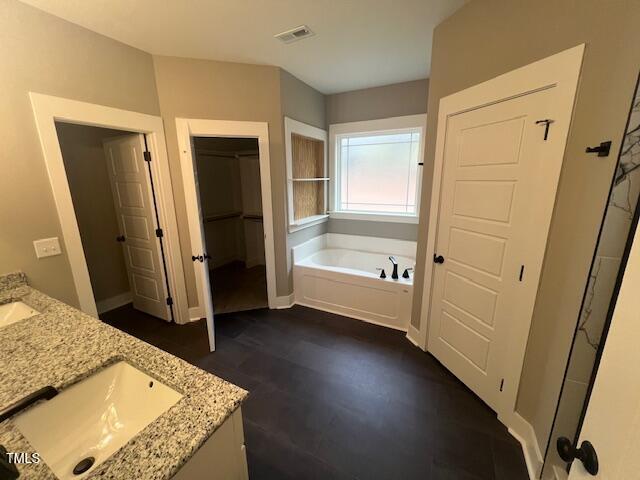 bathroom with visible vents, a sink, wood finished floors, double vanity, and a bath