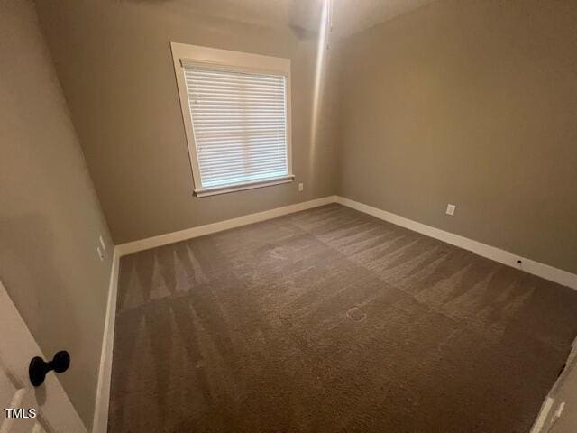 unfurnished room featuring baseboards and dark colored carpet