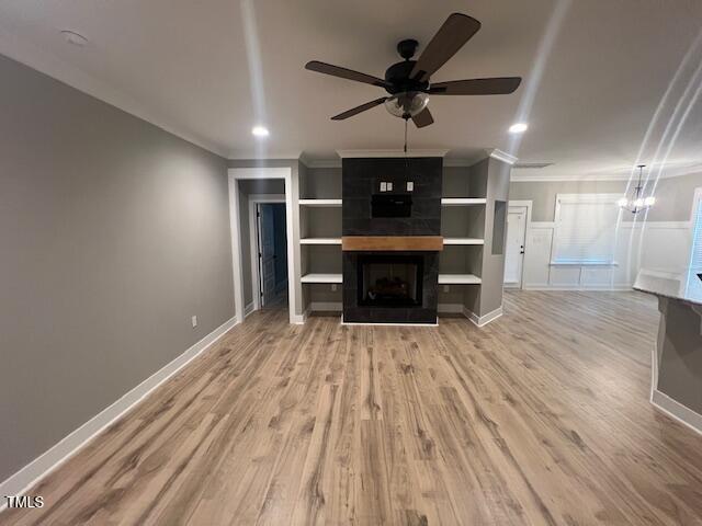 unfurnished living room with wood finished floors, baseboards, crown molding, ceiling fan with notable chandelier, and a large fireplace