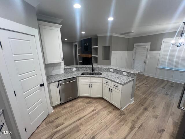 kitchen with a peninsula, a sink, white cabinets, light wood-style floors, and stainless steel dishwasher