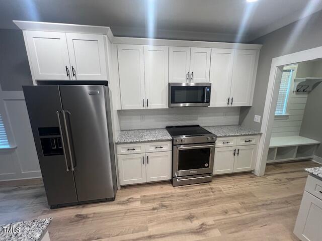 kitchen with light stone countertops, light wood-style flooring, stainless steel appliances, white cabinetry, and tasteful backsplash