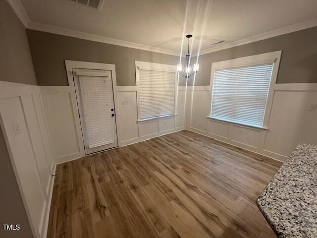 unfurnished dining area with a chandelier, wood finished floors, ornamental molding, and a decorative wall