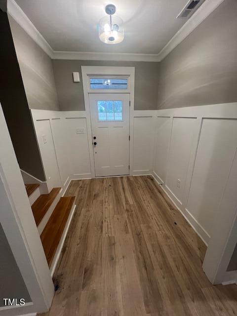 foyer featuring visible vents, a wainscoted wall, ornamental molding, wood finished floors, and a decorative wall