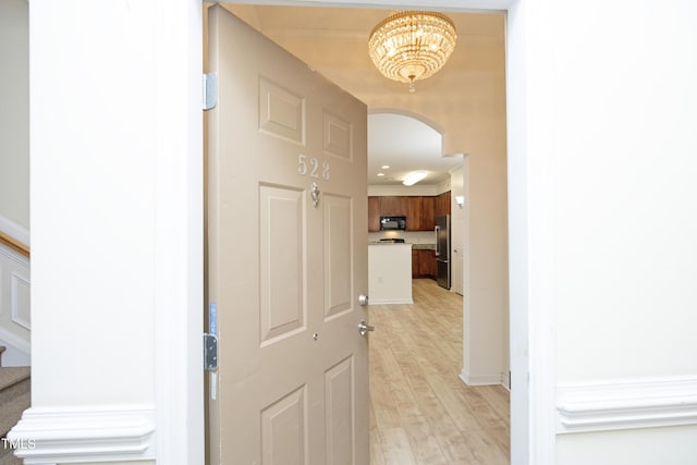 corridor with arched walkways, baseboards, stairs, and light wood-style floors