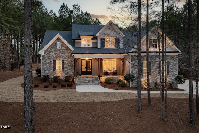 view of front facade featuring stone siding, a porch, and french doors