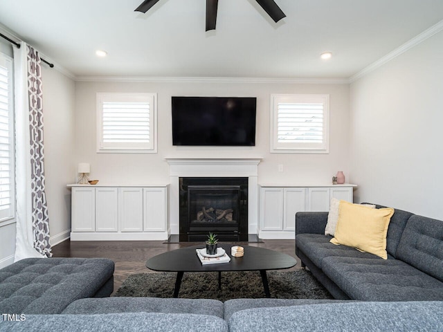 living room with plenty of natural light, dark wood-type flooring, crown molding, and a glass covered fireplace