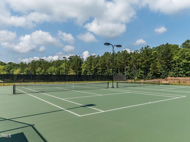 view of tennis court featuring a forest view and fence