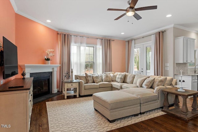 living area with dark wood-style floors, recessed lighting, a glass covered fireplace, and crown molding