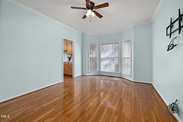 empty room with crown molding, ceiling fan, wood-type flooring, and baseboards