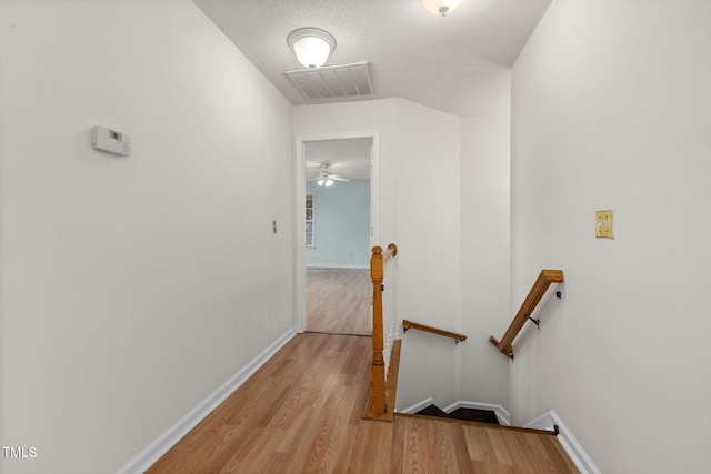 hallway with light wood-type flooring, baseboards, visible vents, and an upstairs landing