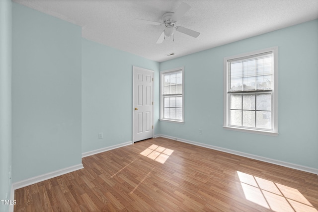 spare room with visible vents, a ceiling fan, a textured ceiling, wood finished floors, and baseboards