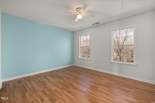 empty room with baseboards, visible vents, a ceiling fan, wood finished floors, and a textured ceiling