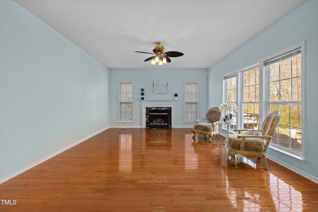 unfurnished room with ceiling fan, a premium fireplace, wood finished floors, and baseboards