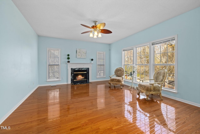 sitting room with a ceiling fan, a premium fireplace, baseboards, and wood finished floors