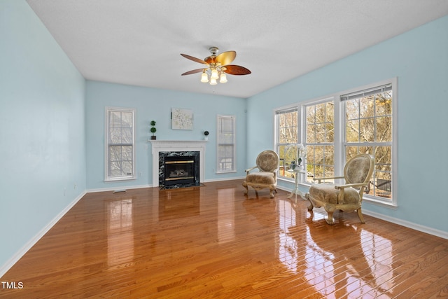 sitting room featuring ceiling fan, wood finished floors, a high end fireplace, and baseboards