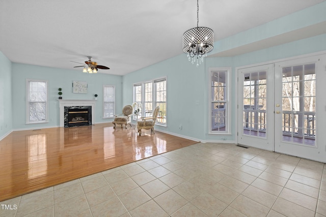 unfurnished living room featuring tile patterned flooring, ceiling fan with notable chandelier, visible vents, a high end fireplace, and baseboards