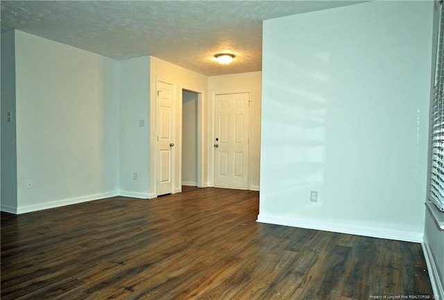 empty room featuring a textured ceiling, dark wood-type flooring, and baseboards