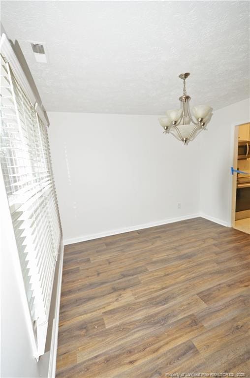 empty room featuring baseboards, a textured ceiling, a chandelier, and wood finished floors