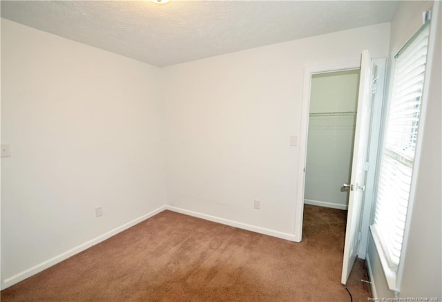 unfurnished bedroom with baseboards, carpet, a spacious closet, a textured ceiling, and a closet