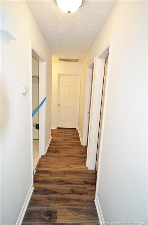 hall featuring visible vents, baseboards, dark wood finished floors, and a textured ceiling