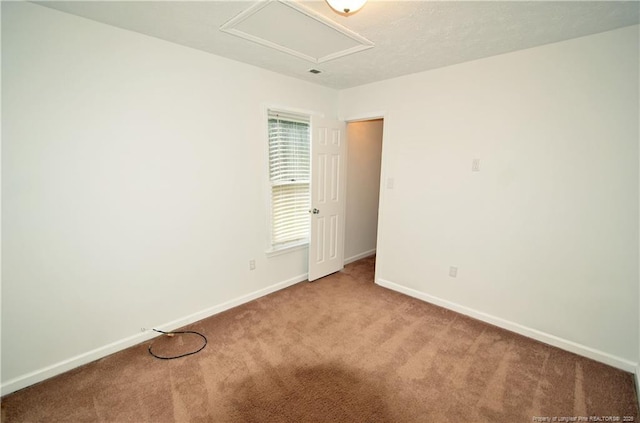 carpeted empty room with attic access and baseboards