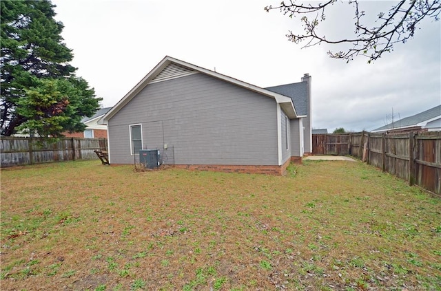 exterior space with a fenced backyard, a yard, a chimney, and central air condition unit