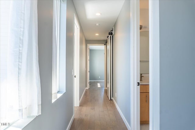 hall featuring a barn door, light wood-type flooring, recessed lighting, and baseboards