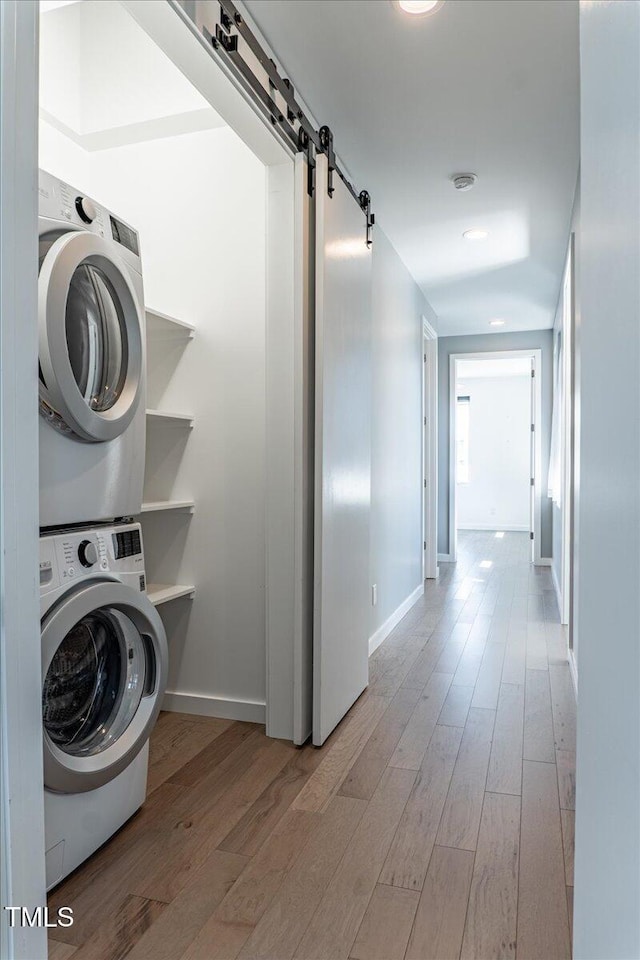 laundry area with a barn door, laundry area, wood finished floors, baseboards, and stacked washer and clothes dryer