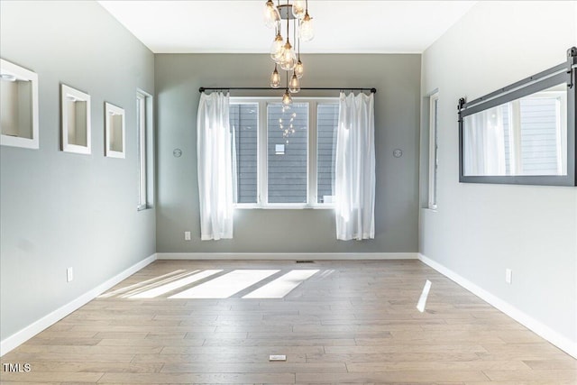 unfurnished dining area featuring baseboards, an inviting chandelier, and wood finished floors