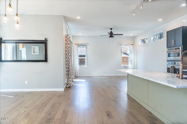 kitchen with light wood finished floors, recessed lighting, stainless steel double oven, open floor plan, and light stone countertops