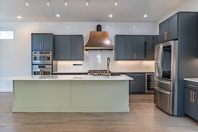 kitchen featuring a center island with sink, wine cooler, appliances with stainless steel finishes, light stone countertops, and extractor fan