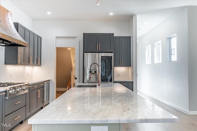 kitchen with light stone counters, range hood, a center island, appliances with stainless steel finishes, and baseboards