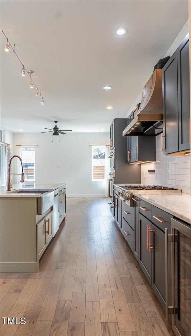 kitchen with stainless steel appliances, decorative backsplash, light wood-type flooring, beverage cooler, and exhaust hood