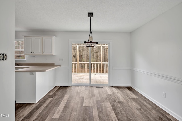 unfurnished dining area with a notable chandelier, a textured ceiling, baseboards, and wood finished floors