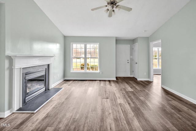 unfurnished living room featuring baseboards, vaulted ceiling, wood finished floors, and a glass covered fireplace