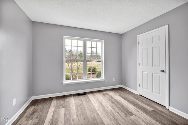 spare room featuring a textured ceiling, wood finished floors, visible vents, and baseboards