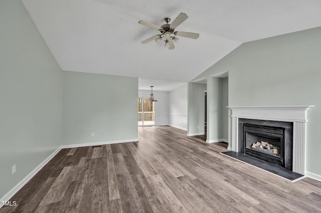 unfurnished living room with ceiling fan with notable chandelier, a fireplace, wood finished floors, baseboards, and vaulted ceiling