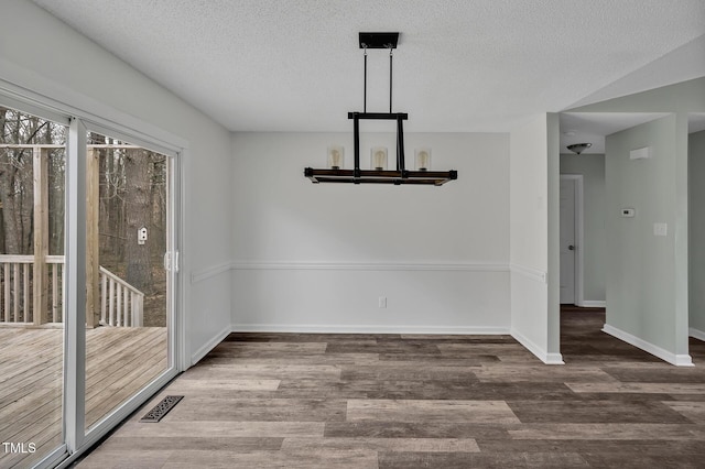 unfurnished dining area with a textured ceiling, wood finished floors, visible vents, and baseboards