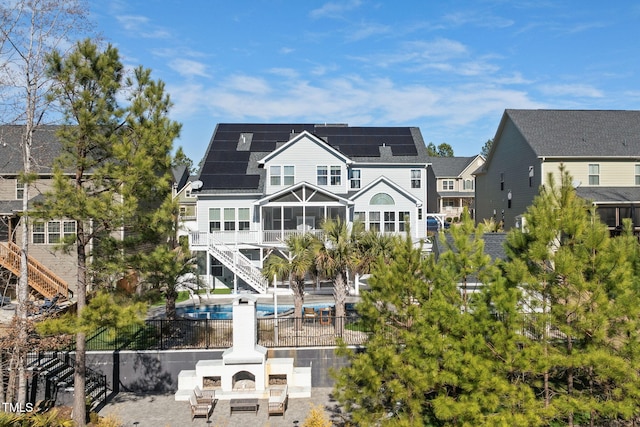 rear view of house featuring a patio, solar panels, a sunroom, stairway, and a fenced in pool