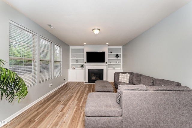 living room with built in shelves, light wood finished floors, visible vents, a fireplace with flush hearth, and baseboards