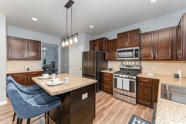 kitchen with decorative light fixtures, light wood finished floors, stainless steel appliances, dark brown cabinets, and a kitchen breakfast bar