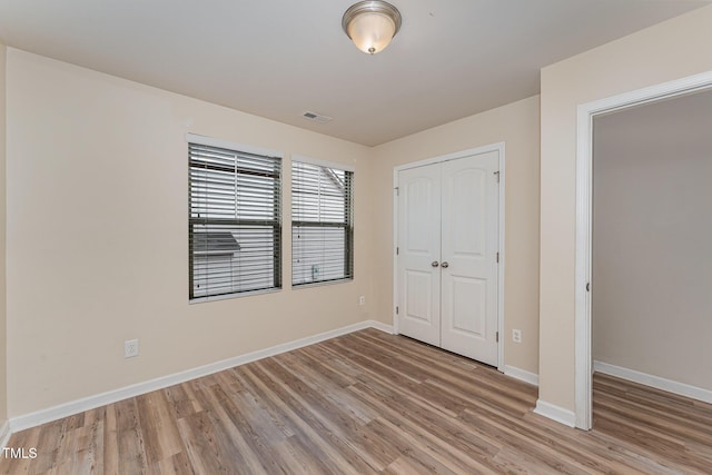 unfurnished bedroom with light wood-type flooring, a closet, visible vents, and baseboards